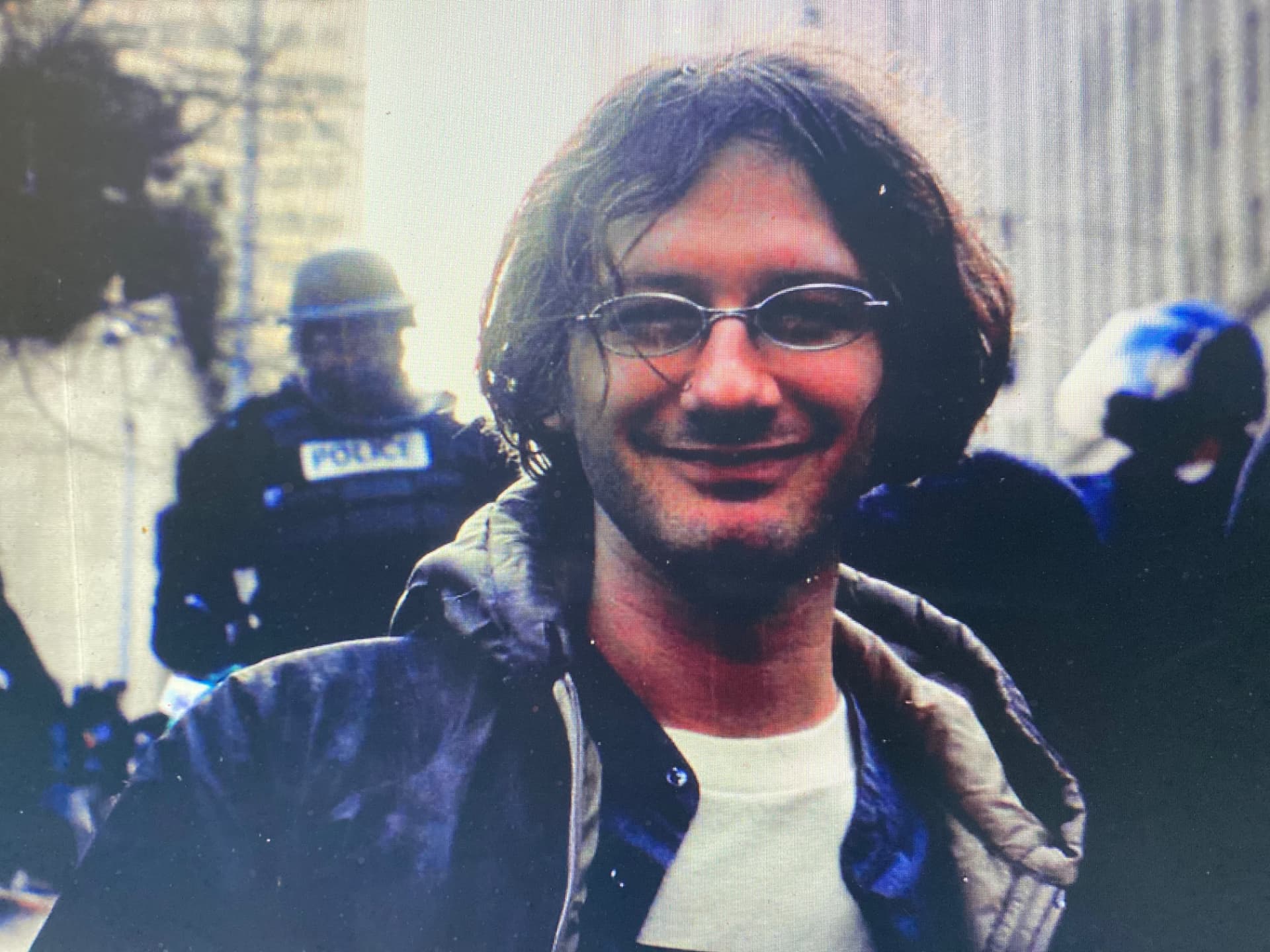 Young Brian Davis smiling in front of riot police on the first day of the 1999 WTO protests in Seattle